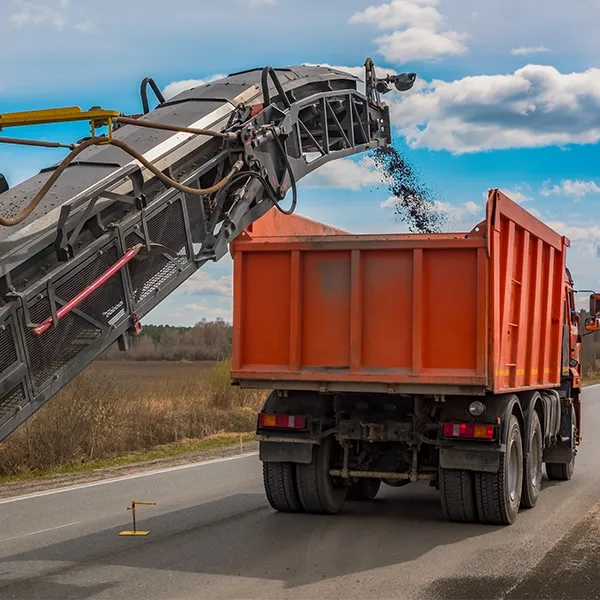 A road reclamation machine is dumping asphalt into a dump truck.