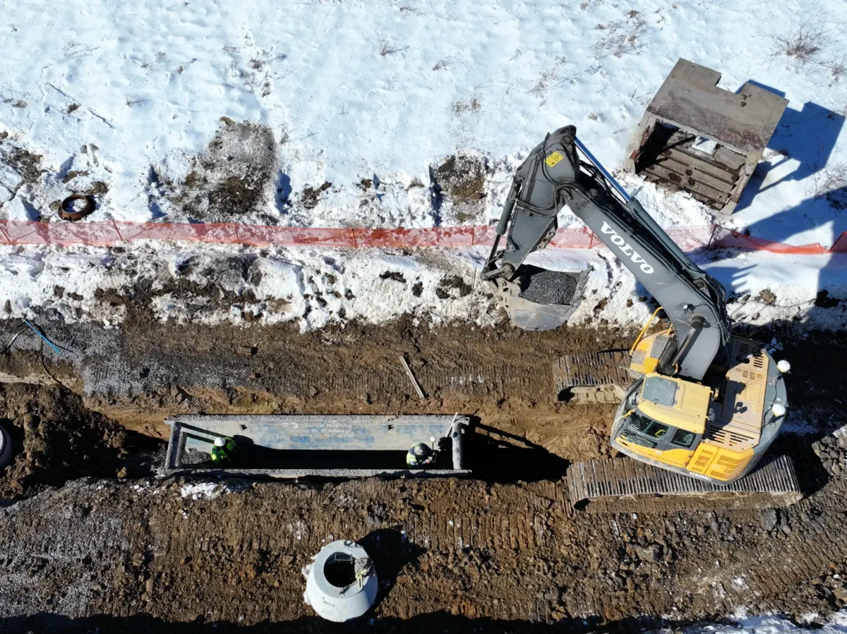 An excavator is digging a hole with snow around it.