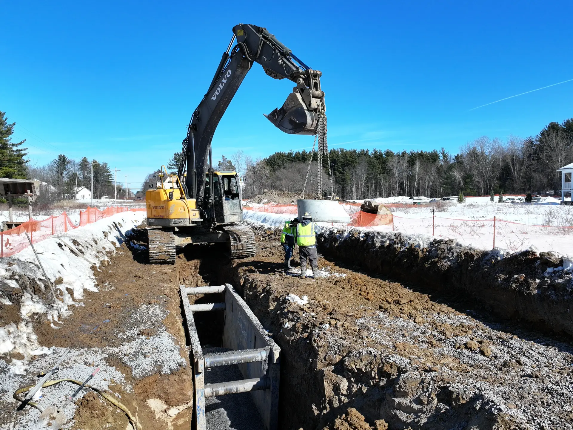 An excavator is digging a hole with an operator nearby.